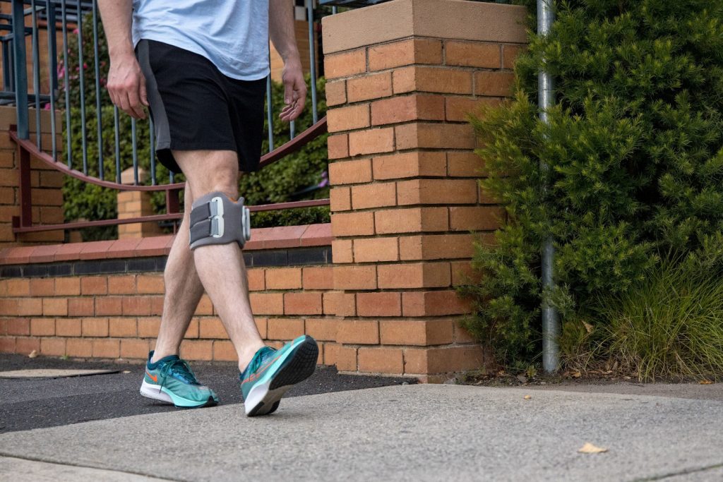 Person walking outdoors wearing a functional electrical stimulation (FES) device below the knee