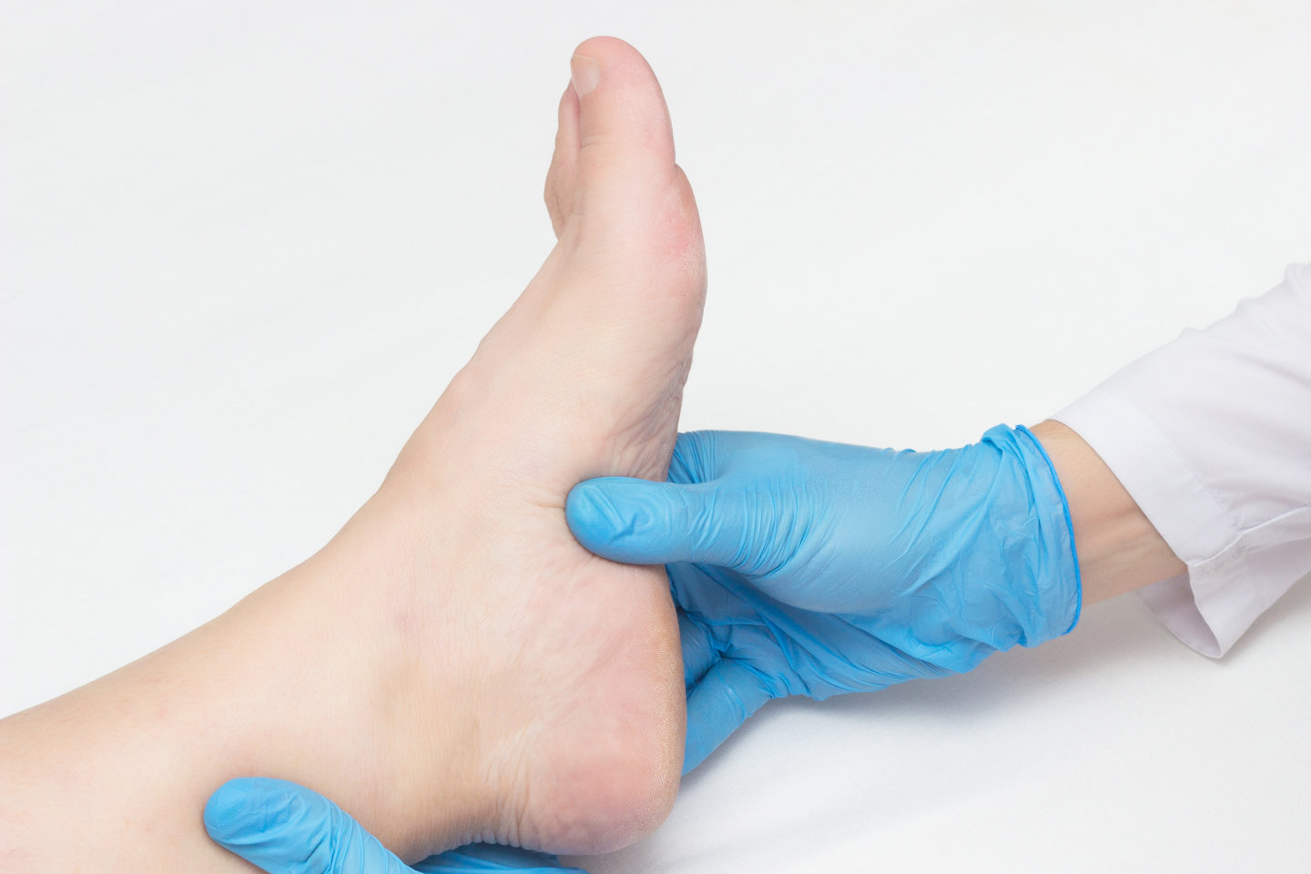 Doctor examines the patient's leg with plantar fasciitis, pain in the foot, white background, close-up, inspection