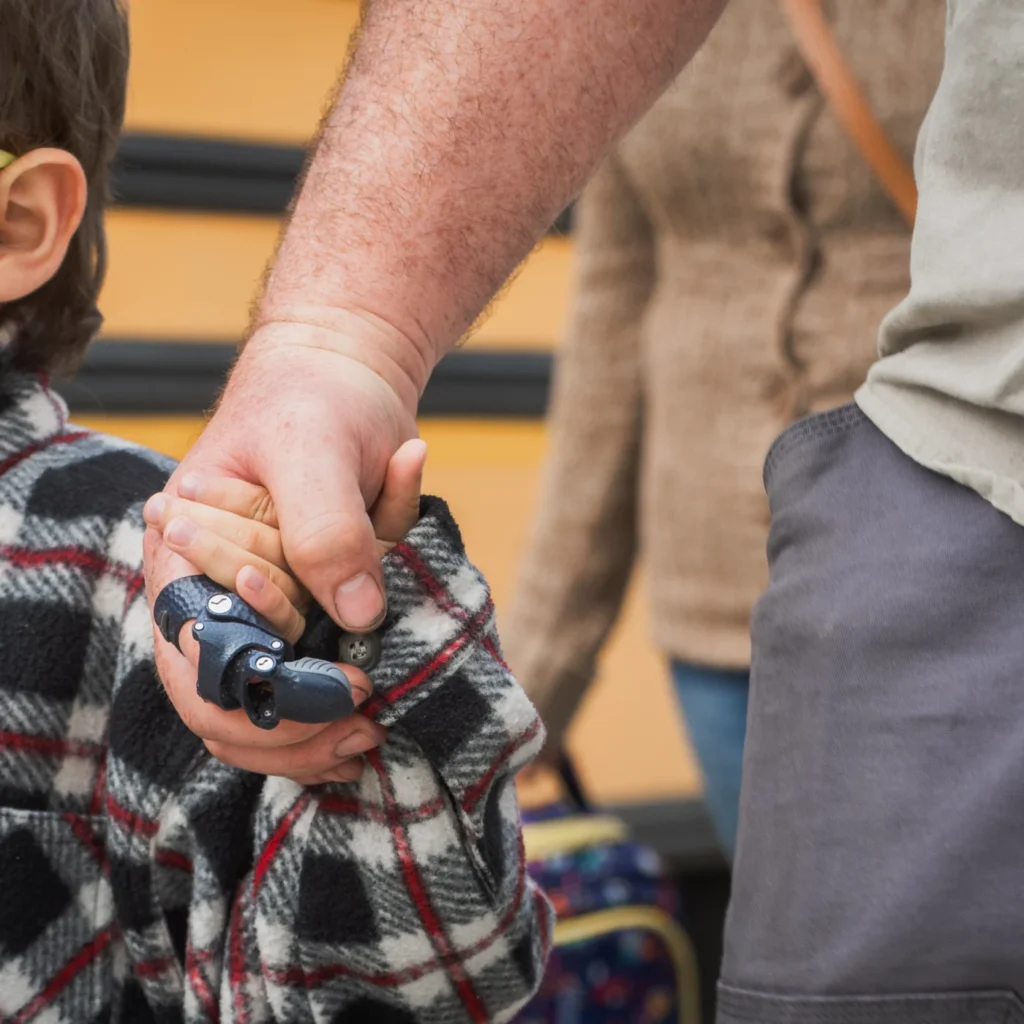 Parent holding a child's hand while wearing a body-powered finger prosthesis