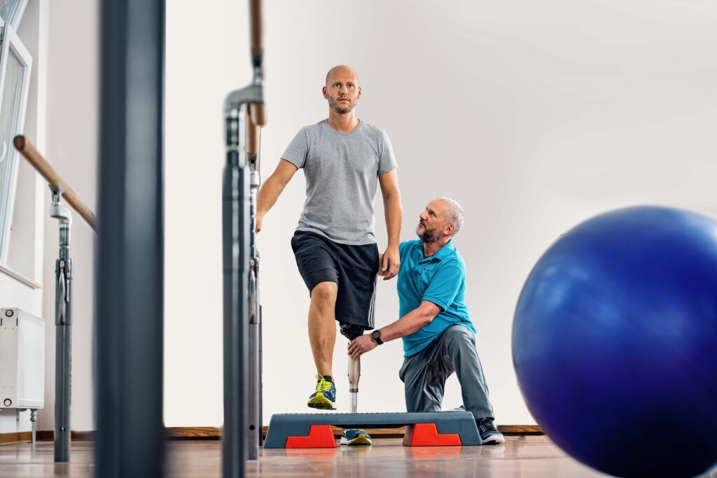 Clinician checking a man's prosthetic leg as he stands at parallel bars